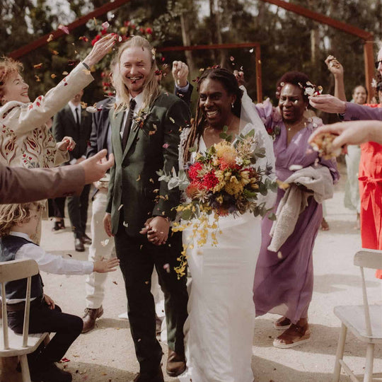 Wedding couple celebrating outdoors with guests, surrounded by trees and a red arch.